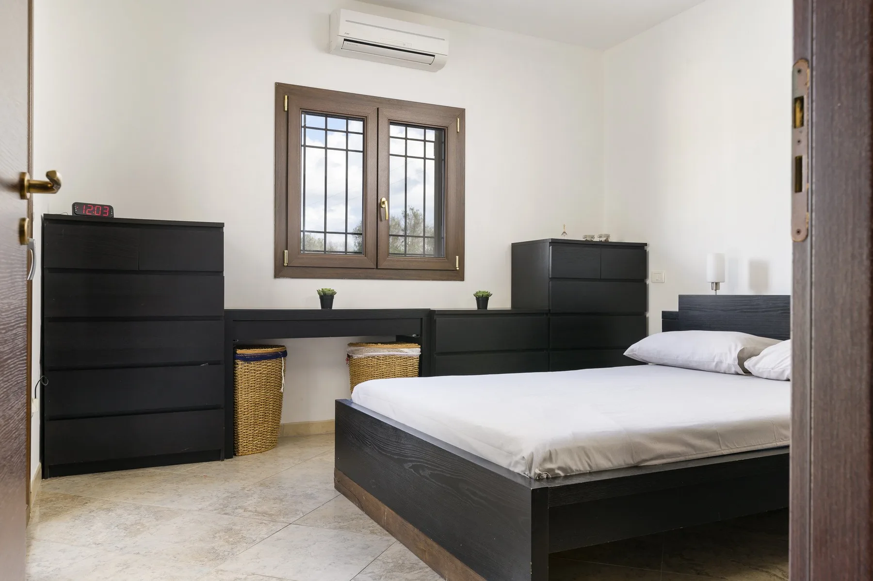 Un dormitorio con una cama, cómodas oscuras y una ventana.