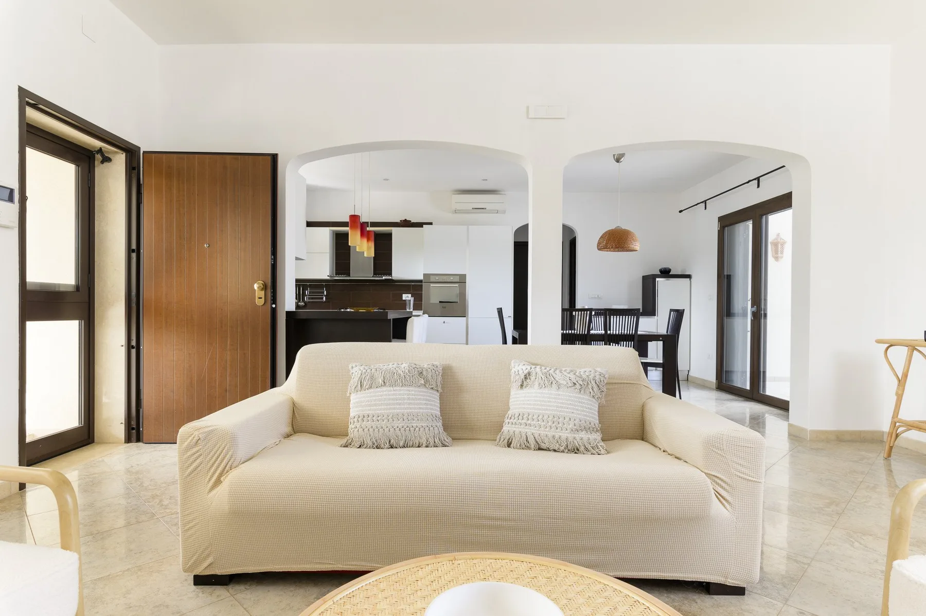 A bright living room with a cream sofa and an open kitchen and dining area beyond.