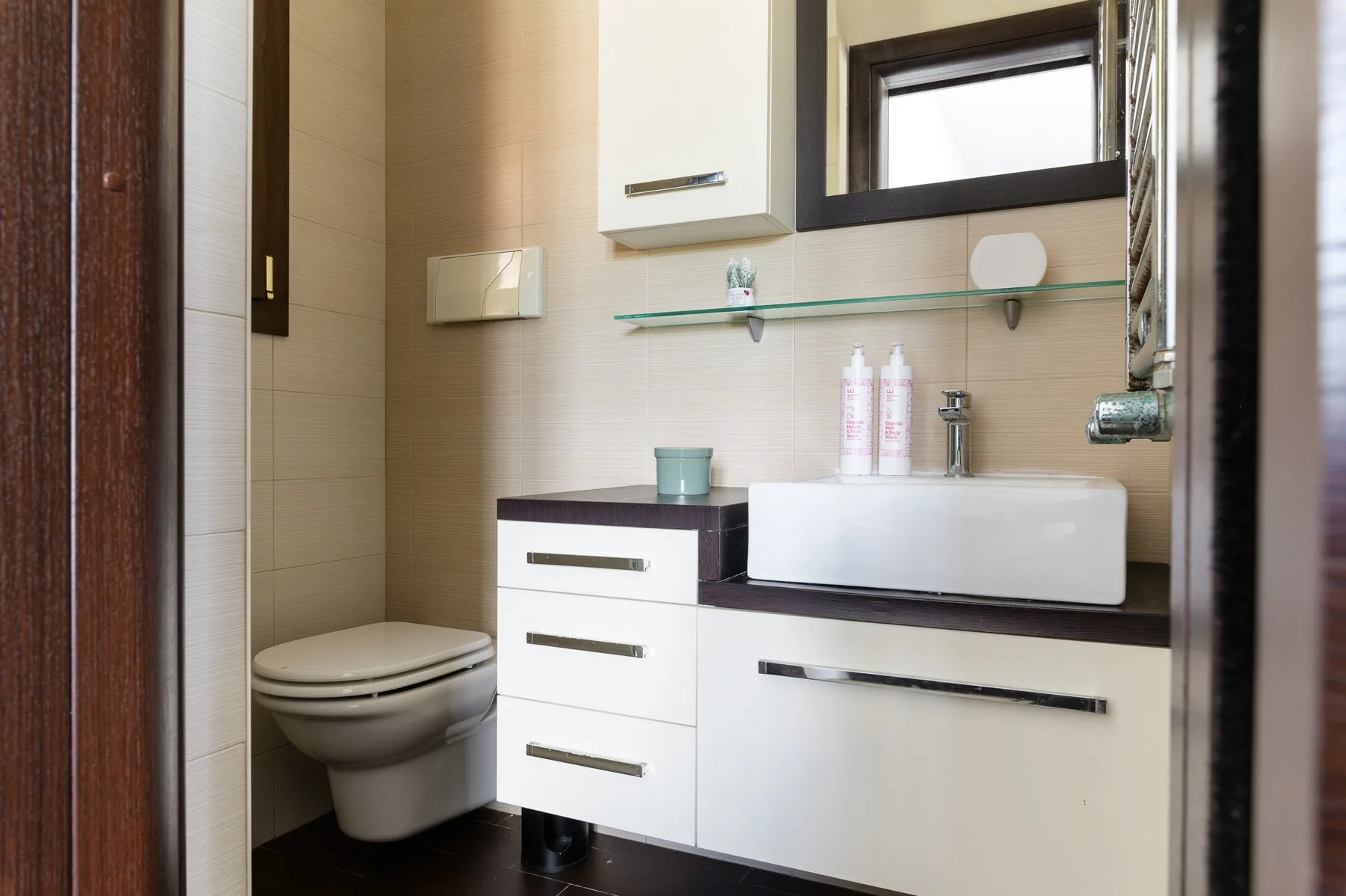Un baño con lavabo, mueble y retrete bajo una ventana.