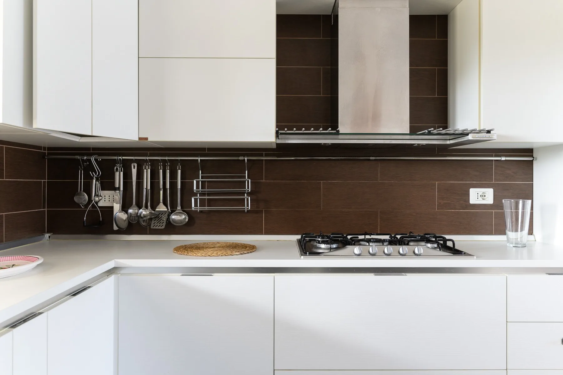 Una cocina moderna con gabinetes blancos, salpicadero oscuro y una estufa de gas.