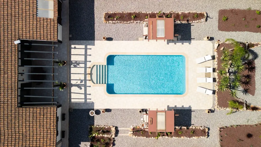 Vista aérea de una piscina al aire libre con tumbonas y asientos cercanos.