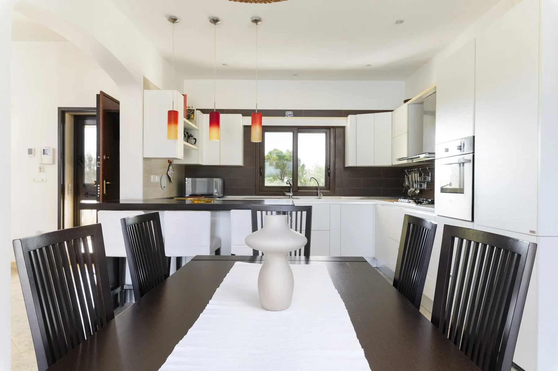 A dining table sits in front of a bright kitchen with white cabinets.