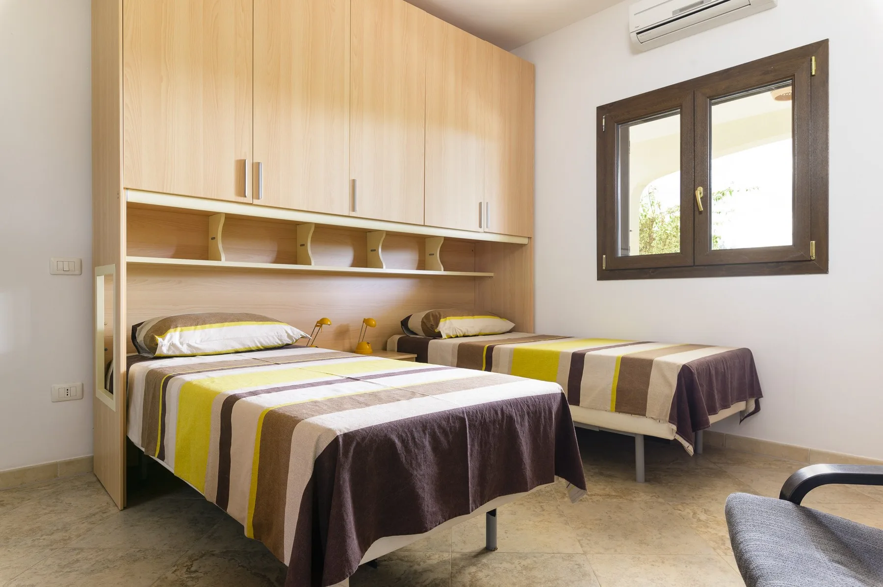 Un dormitorio con dos camas bajo armarios y estantes de madera clara.