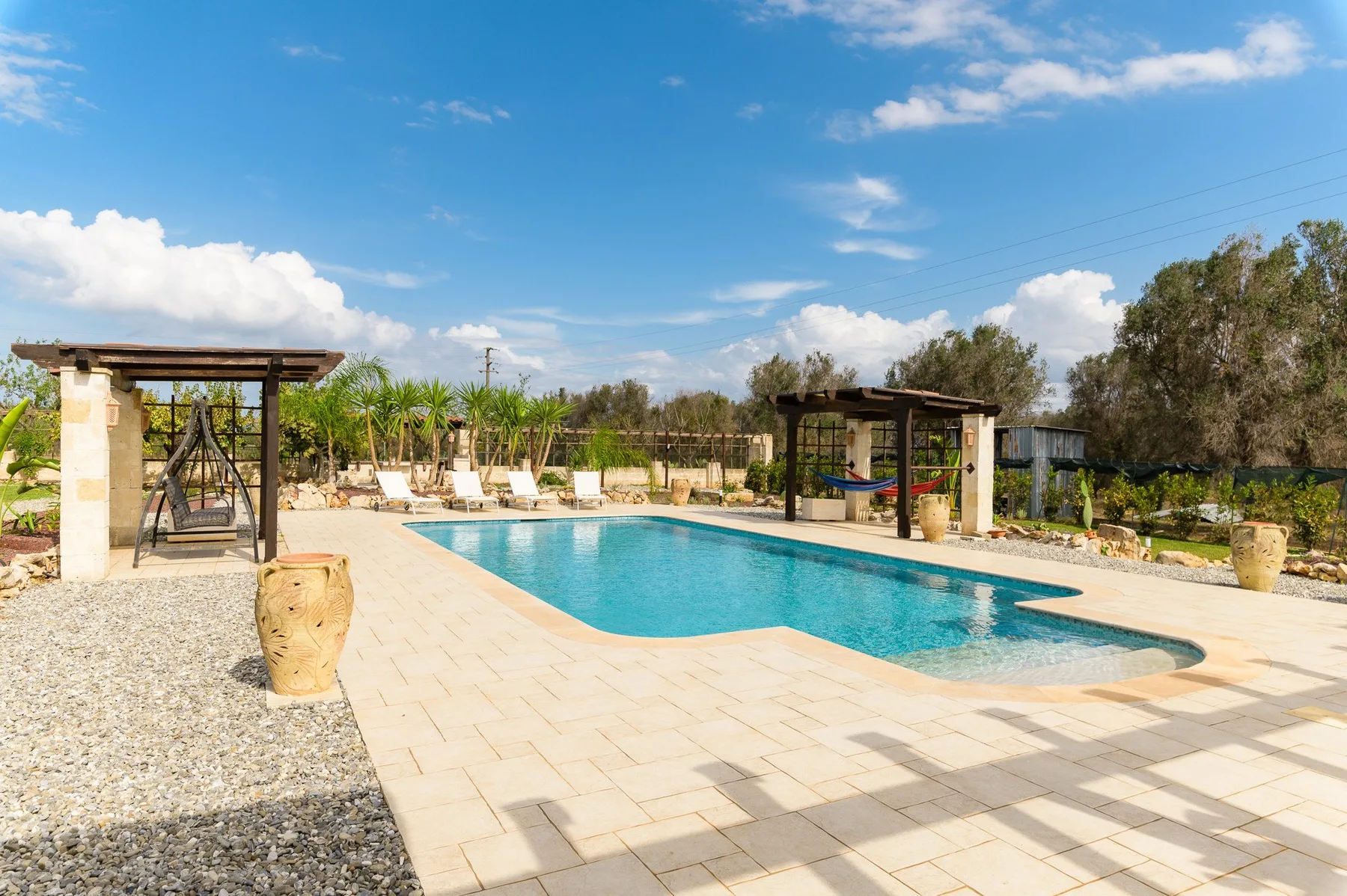 An outdoor swimming pool with a paved deck and shaded seating areas.