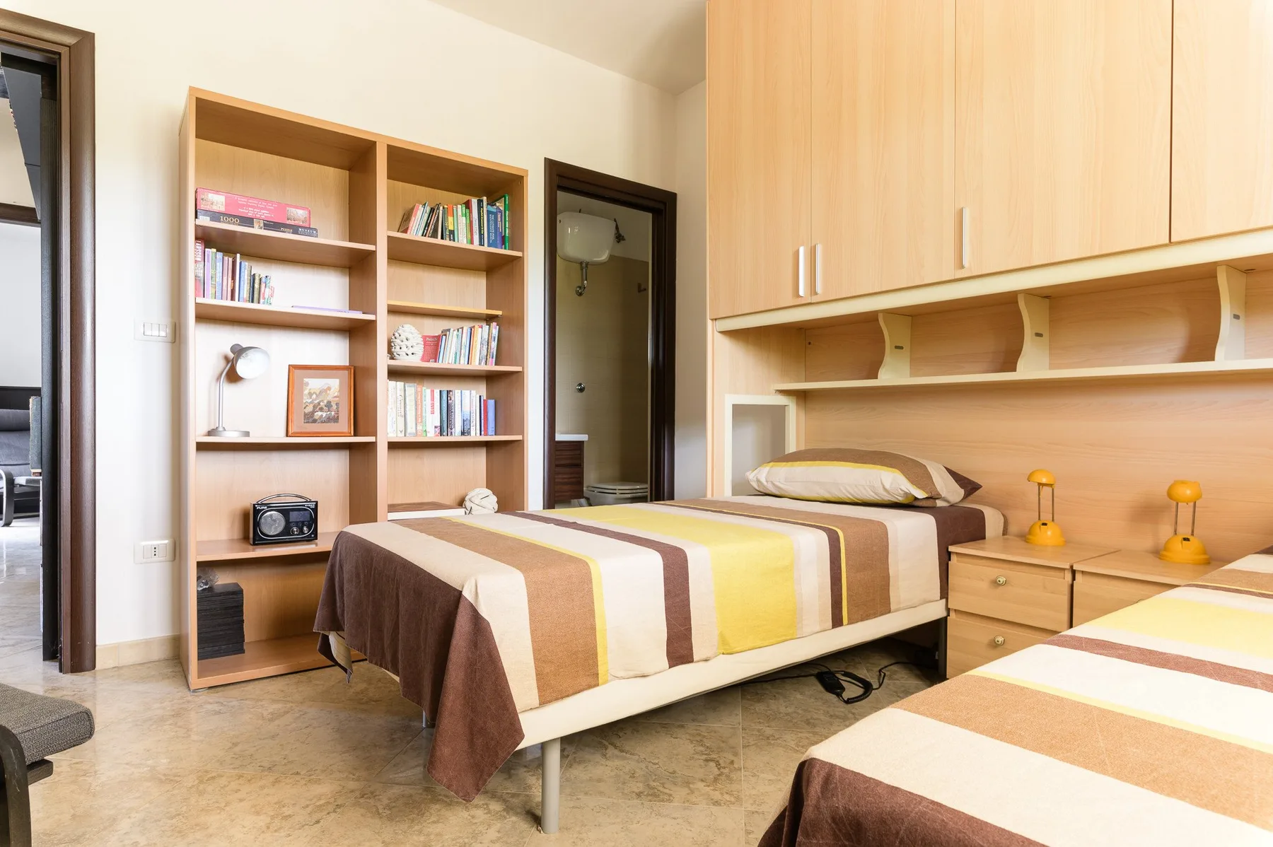 Un dormitorio con camas, armarios empotrados y una estantería.