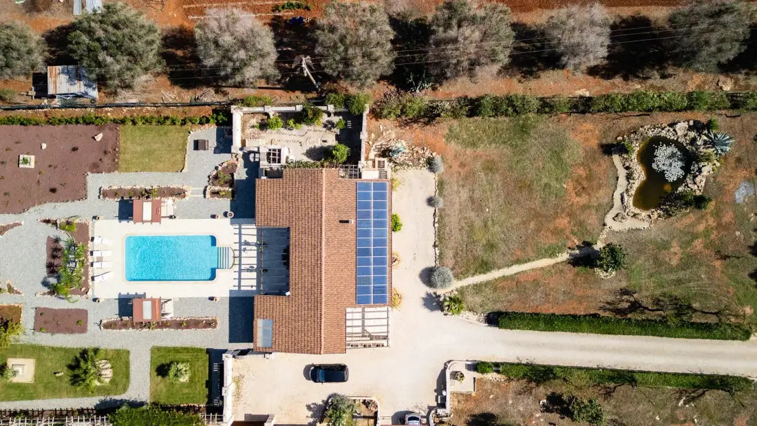 Una vista aérea muestra una propiedad con piscina, paneles solares y terreno alrededor.