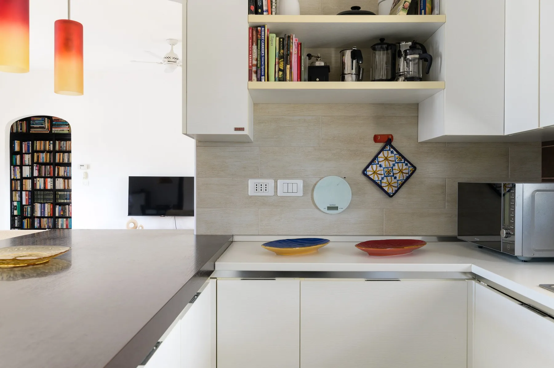 Una cocina moderna y luminosa con armarios blancos, una encimera y estantes abiertos.