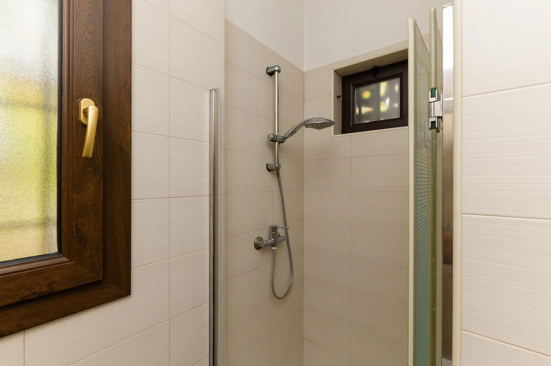 Una ducha de baño con azulejos, una alcachofa y controles en la pared.