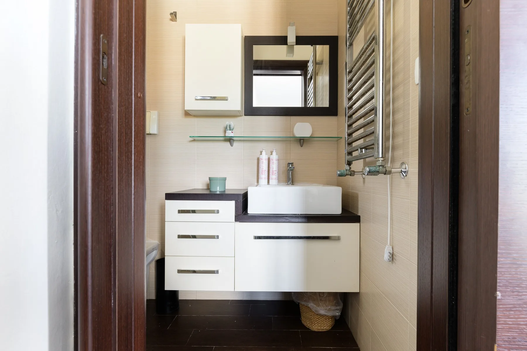Un baño compacto con lavabo, espejo y toallero calefactor de pared.