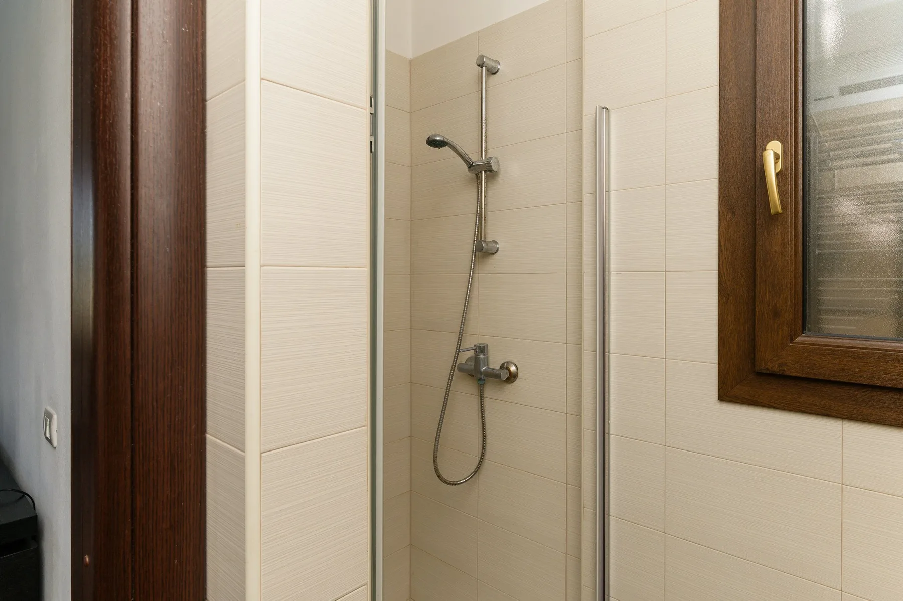 Una ducha de baño con azulejos, ducha de mano y panel de vidrio.