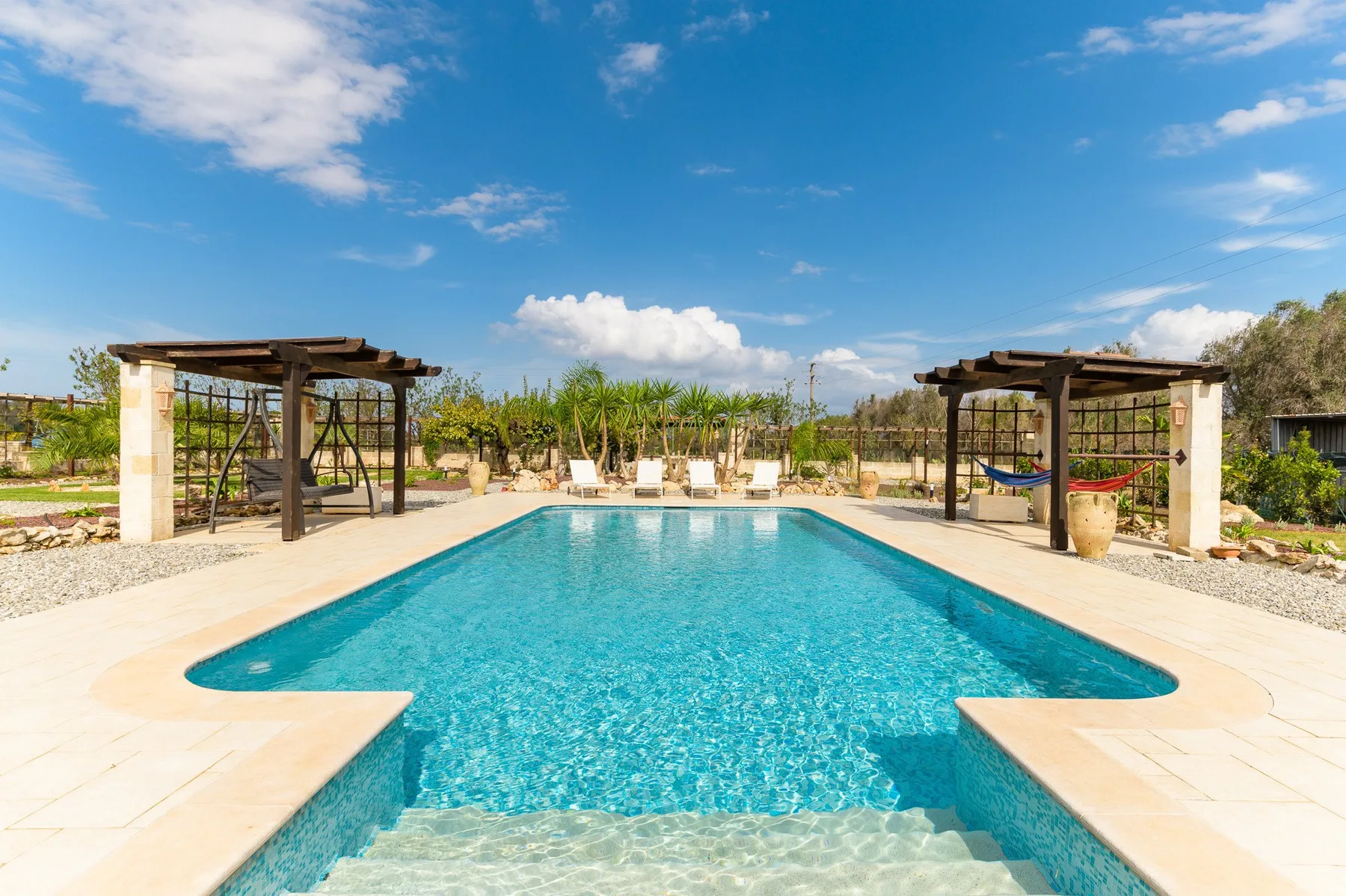Una piscina al aire libre está rodeada por un patio pavimentado y pérgolas.