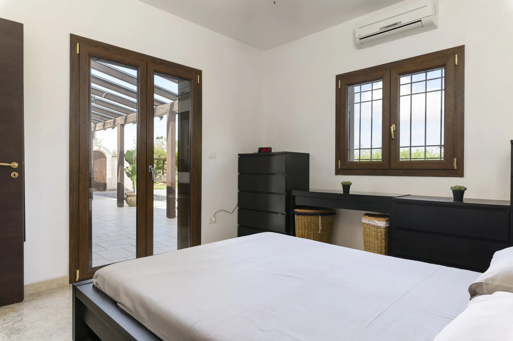 Un dormitorio con una cama, ventanas con marcos de madera oscura y una cómoda baja.