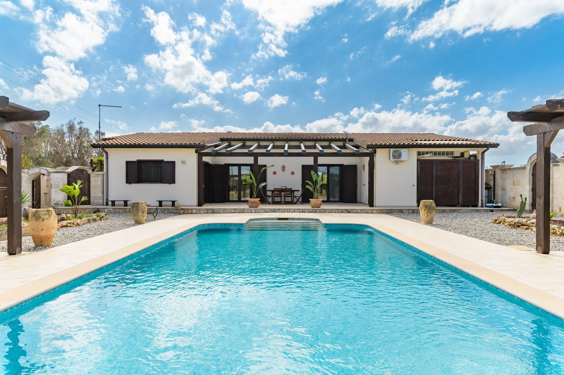 Una piscina frente a una casa de una planta bajo un cielo azul.