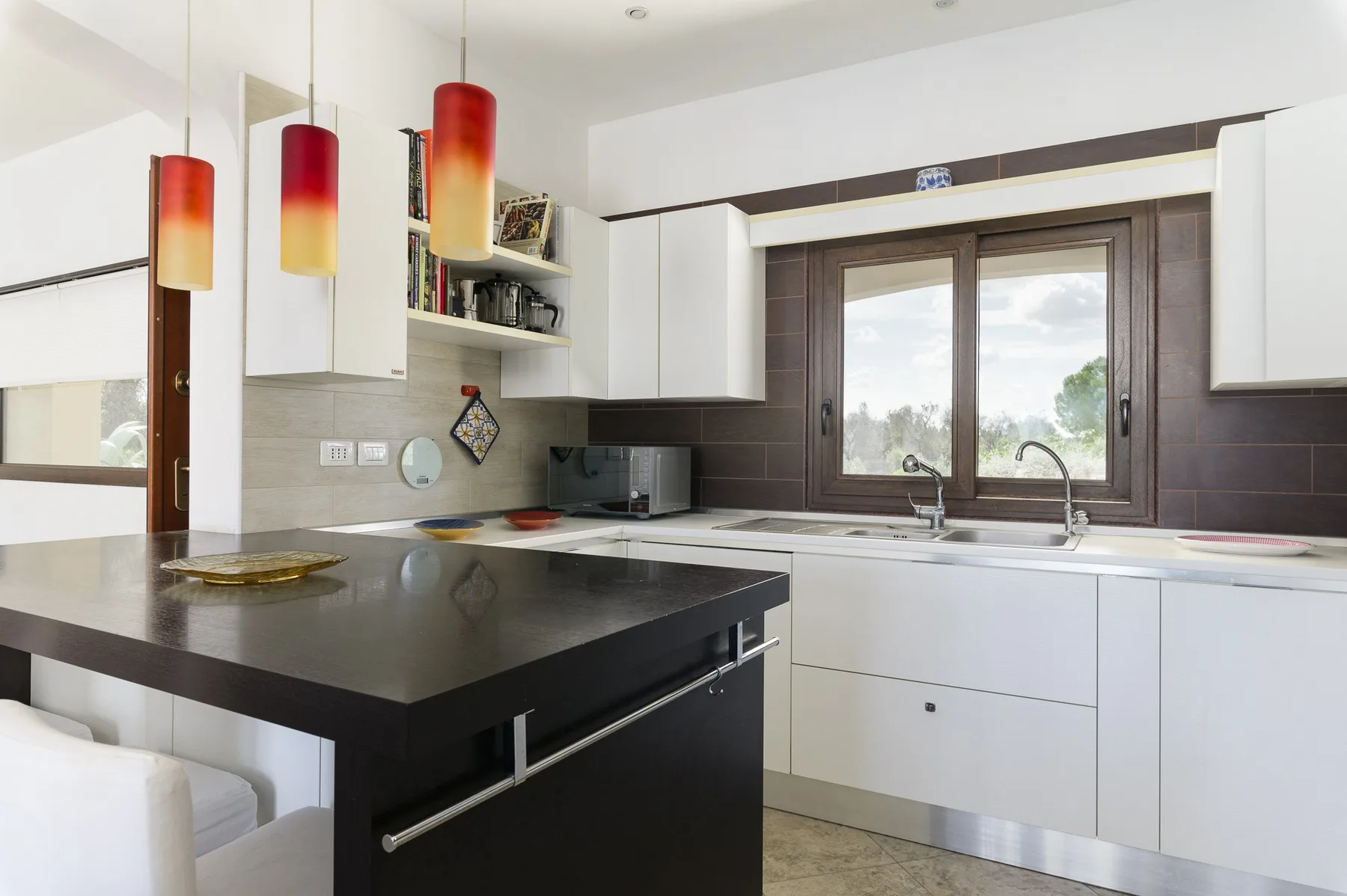 Una cocina luminosa con armarios blancos, una isla oscura y una ventana sobre el fregadero.
