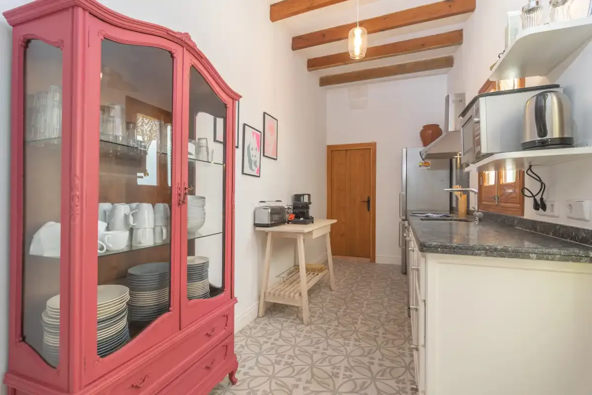 Una cocina luminosa con un armario rojo con puertas de cristal y vigas de madera.