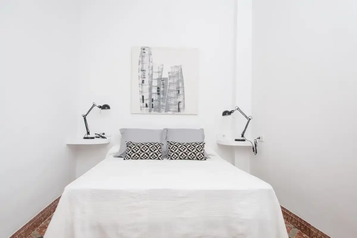Un dormitorio luminoso con una cama bien hecha y lámparas a ambos lados.