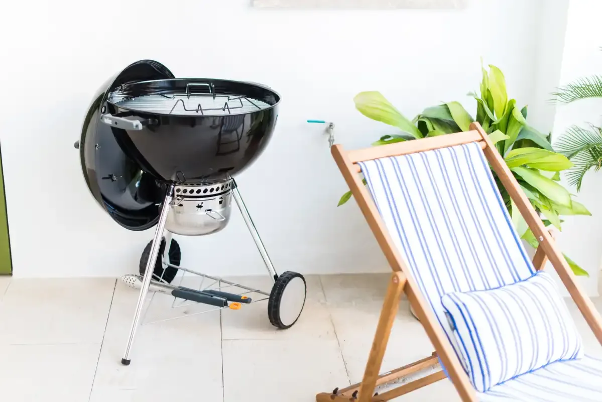 Una zona de descanso en el patio con una silla a rayas junto a una parrilla.