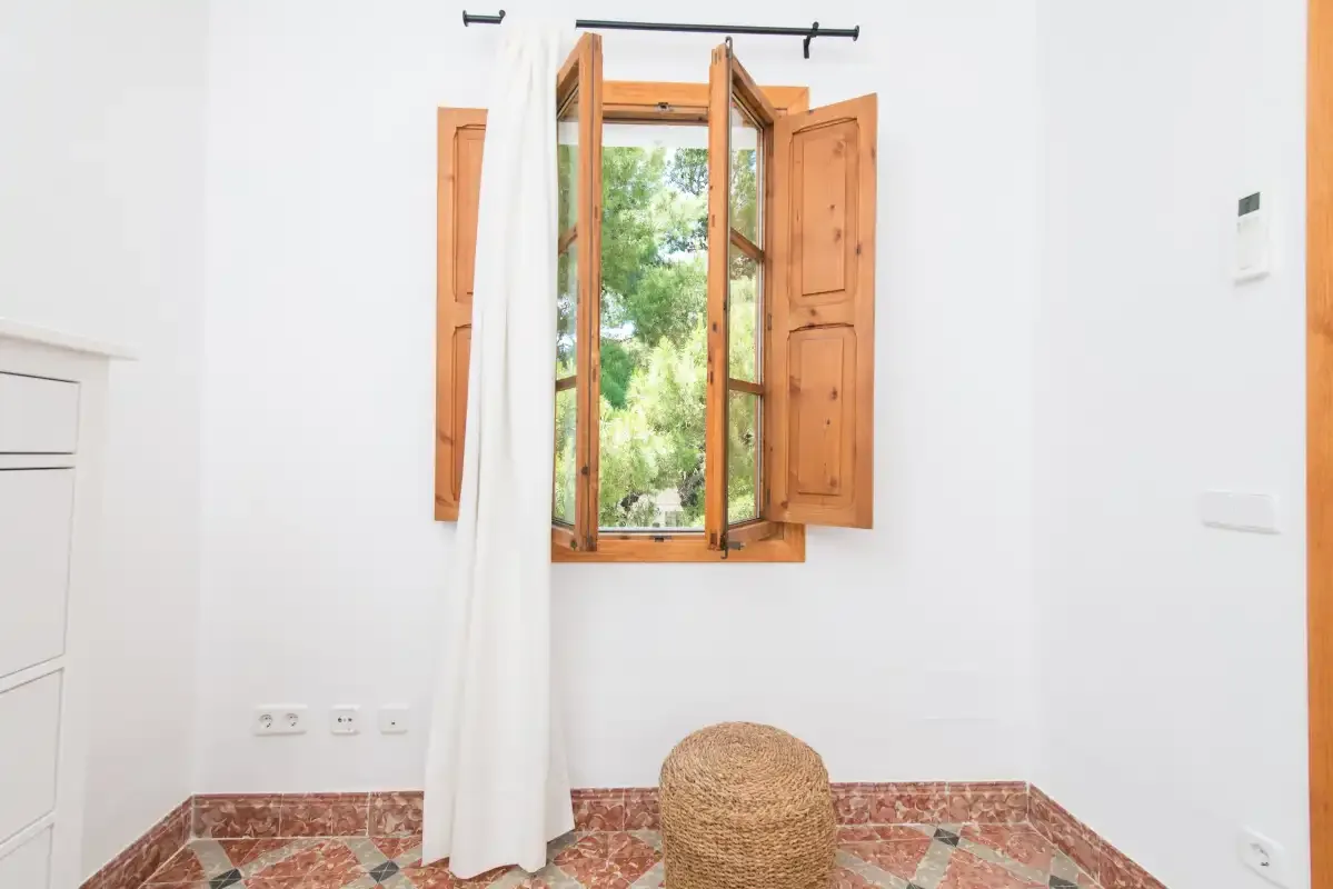 Una habitación luminosa con una ventana de madera abierta y una cesta tejida en el suelo.