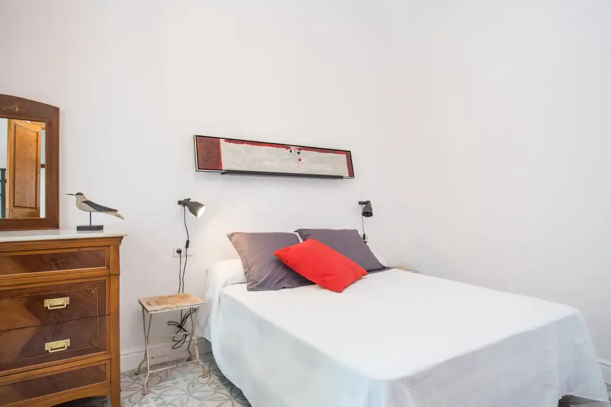 Un dormitorio con una cama bien hecha y una cómoda de madera al lado.