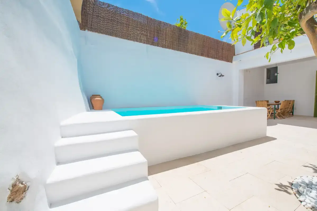 Una pequeña piscina exterior está junto a un patio blanco con escalones y vegetación.