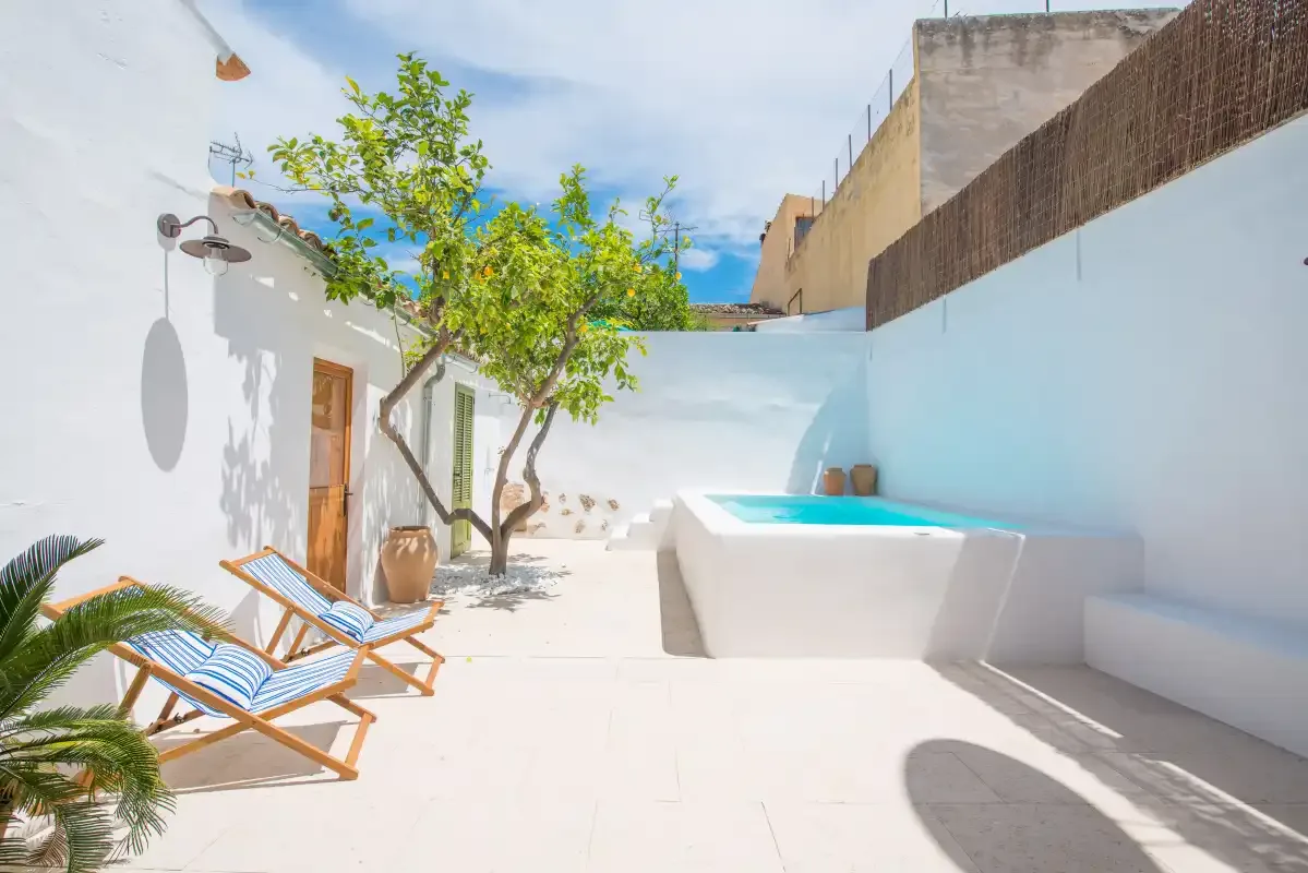 Un patio soleado con una pequeña piscina, tumbonas y un árbol frondoso.