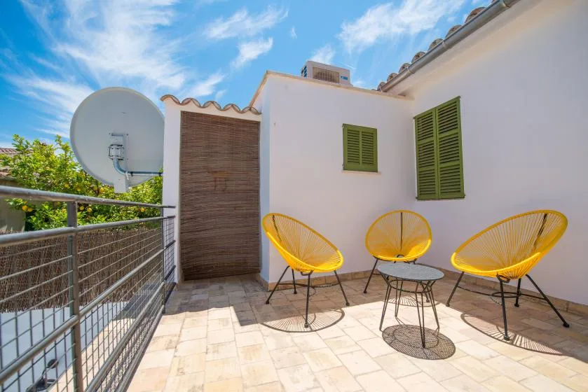Una terraza soleada con asientos amarillos junto a una pared exterior blanca.