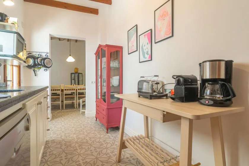 Una cocina luminosa con una encimera, pequeños electrodomésticos y un comedor al fondo.