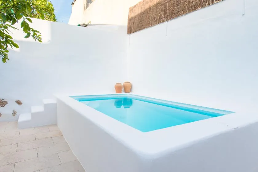 Una pequeña piscina exterior está junto a paredes blancas en un patio pavimentado.