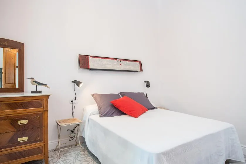 Un dormitorio con una cama bien tendida, almohadas de colores y una cómoda de madera.