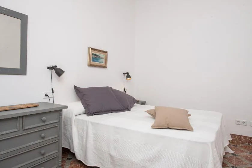 Un dormitorio con una cama blanca, almohadas y una cómoda gris.