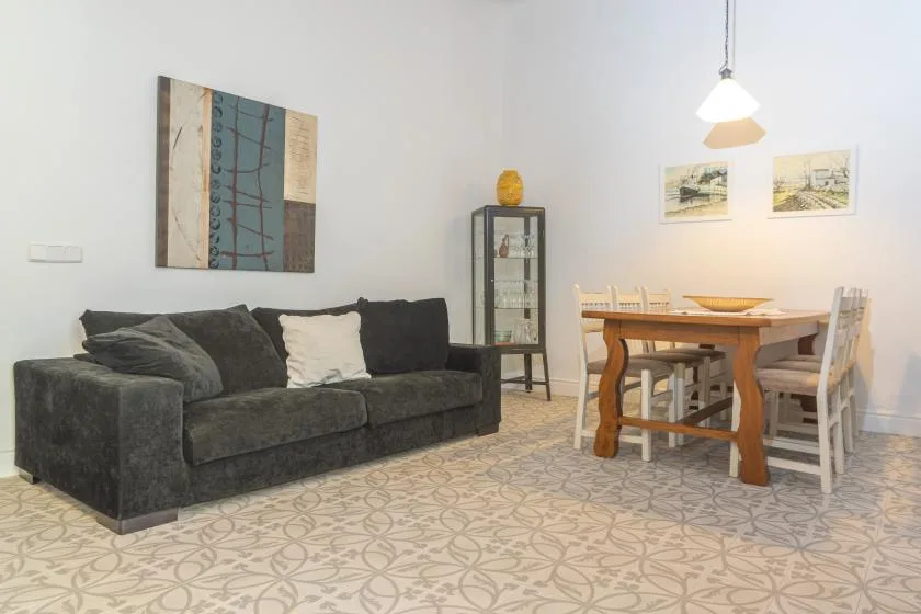 Una zona de estar y comedor con asientos oscuros, una mesa de madera y suelo de baldosas estampadas.
