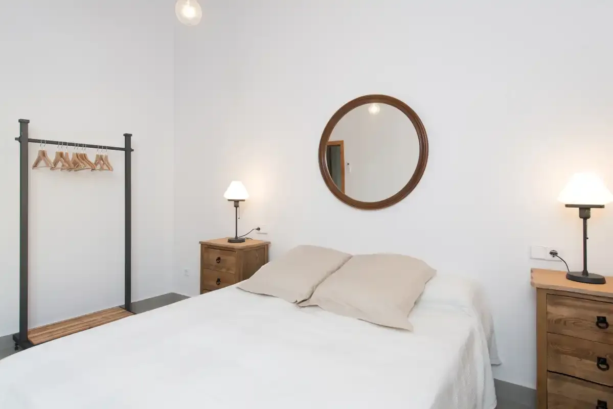 Un dormitorio con una cama bien hecha y un espejo redondo en la pared.