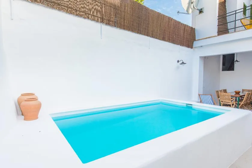 Una piscina luminosa en un patio está junto a una zona de estar cubierta.