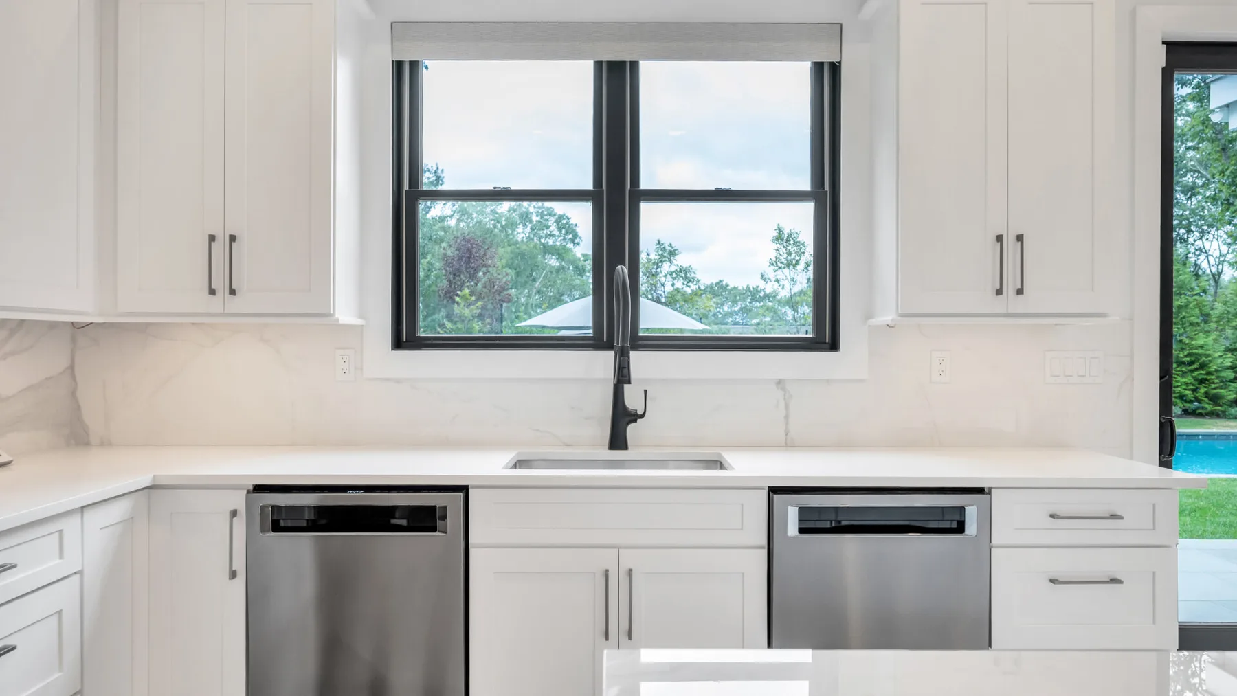 Una cocina luminosa con gabinetes blancos y una ventana grande sobre el fregadero.