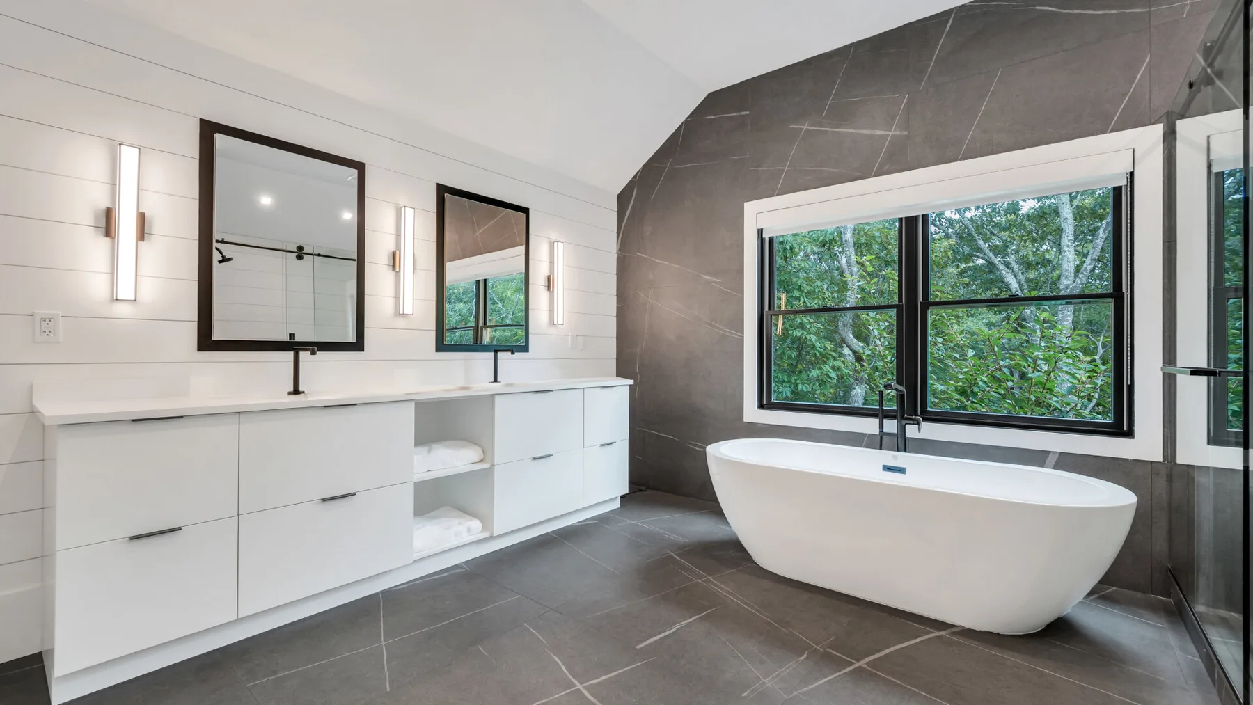 Un baño moderno con una bañera exenta junto a una ventana grande.