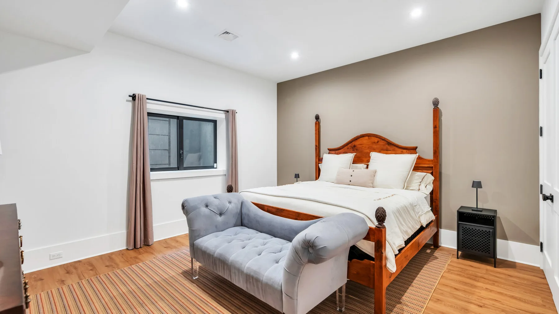 Un dormitorio con una cama de madera y un banco tapizado gris a sus pies.