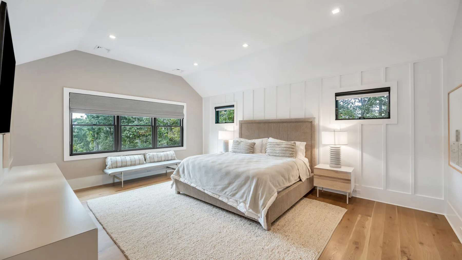 Un dormitorio luminoso con una cama, un banco y grandes ventanas.