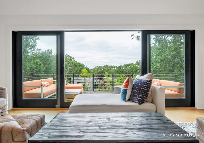 Un dormitorio da a un balcón con asientos al aire libre y vistas arboladas.