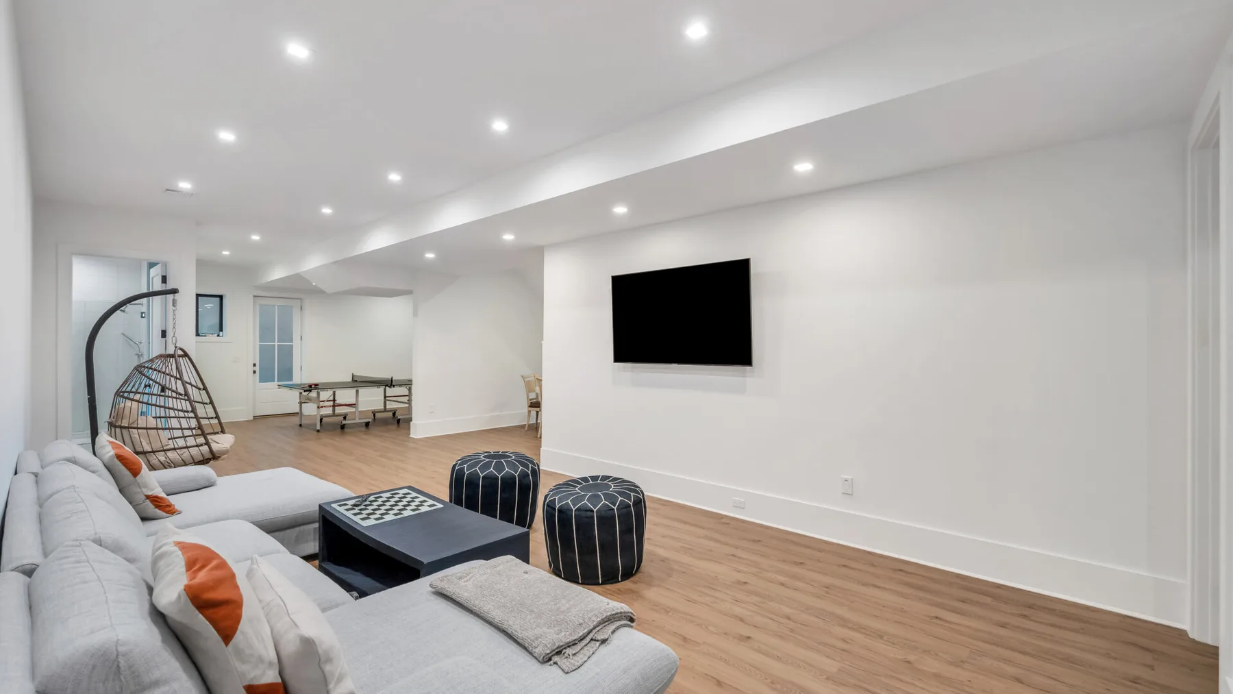 Una sala de estar luminosa con asientos grises, una mesa de centro y un televisor en la pared.