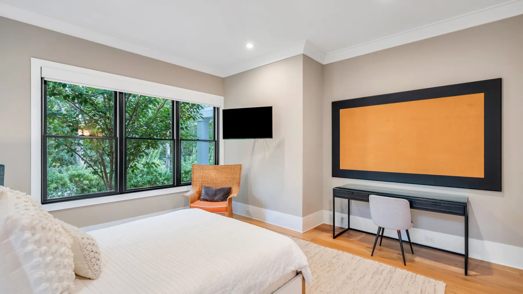 Un dormitorio luminoso con una ventana grande, una cama y un escritorio junto a la pared.