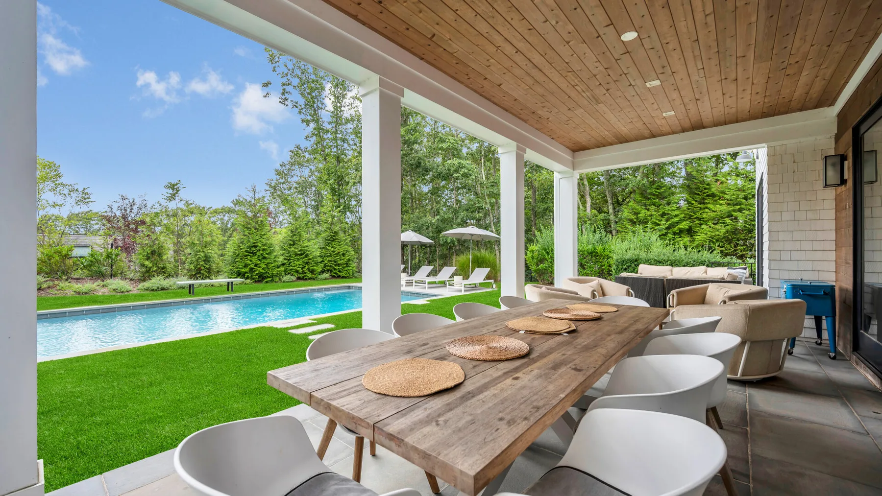 Una zona de comedor cubierta al aire libre da a una piscina y un césped verde.