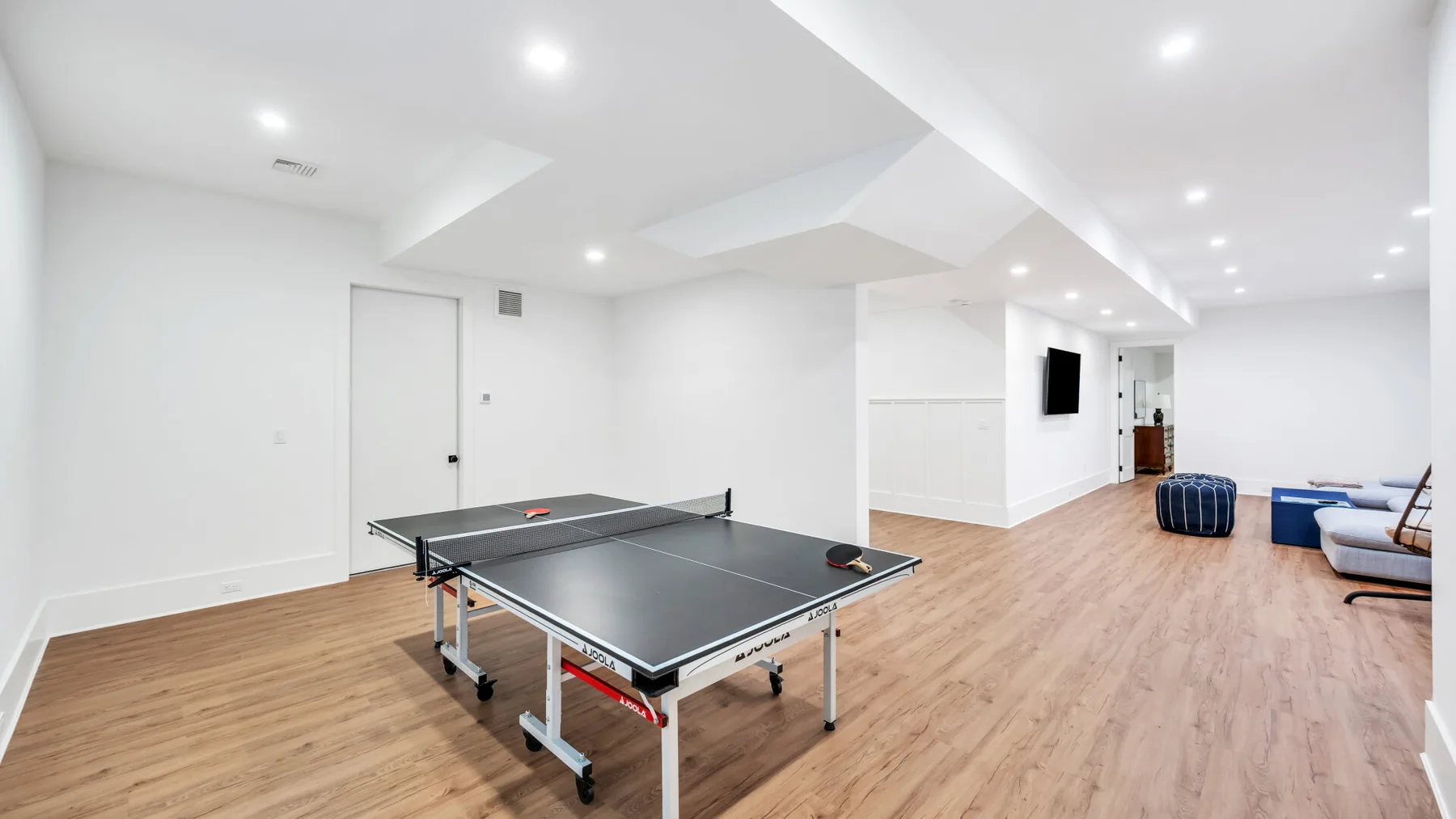 Una amplia y luminosa sala de juegos con una mesa de ping-pong y piso de madera.