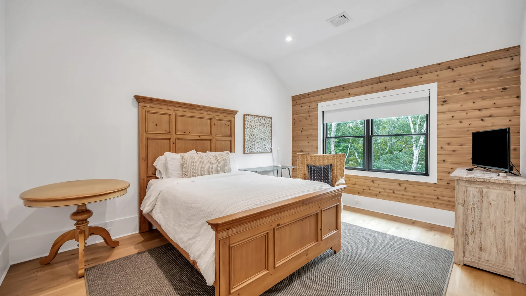 Un dormitorio con una cama de madera, una ventana amplia y un televisor.