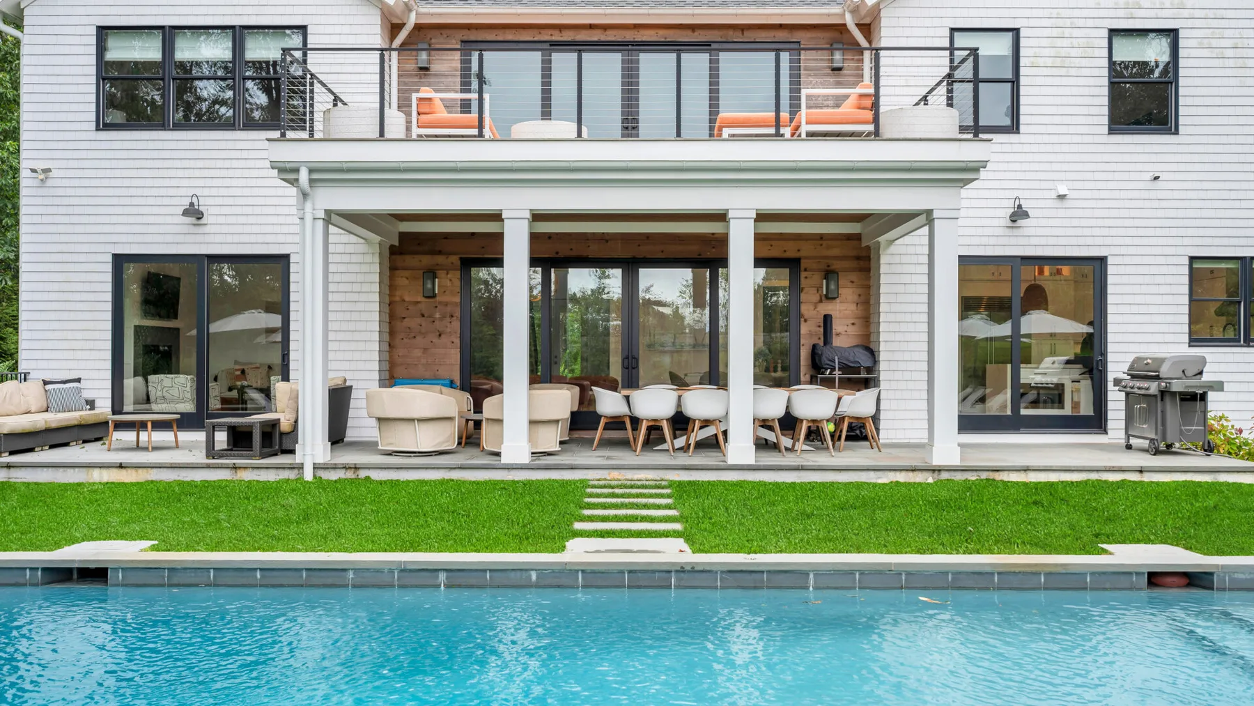 Una casa moderna da a un patio cubierto junto a una piscina y un césped.