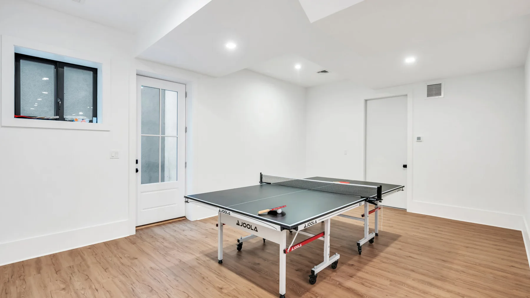 Una habitación luminosa con una mesa de ping-pong y suelo de aspecto madera.