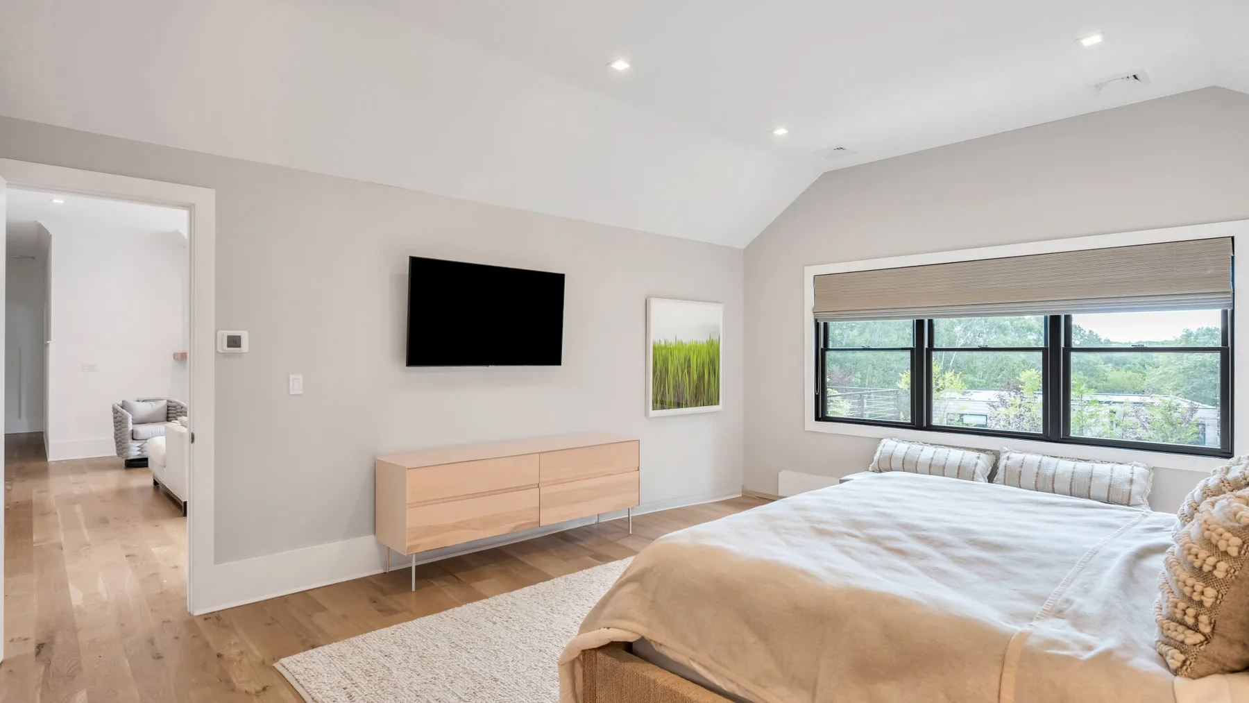 Un dormitorio luminoso con una cama, un televisor en la pared y ventanas amplias.