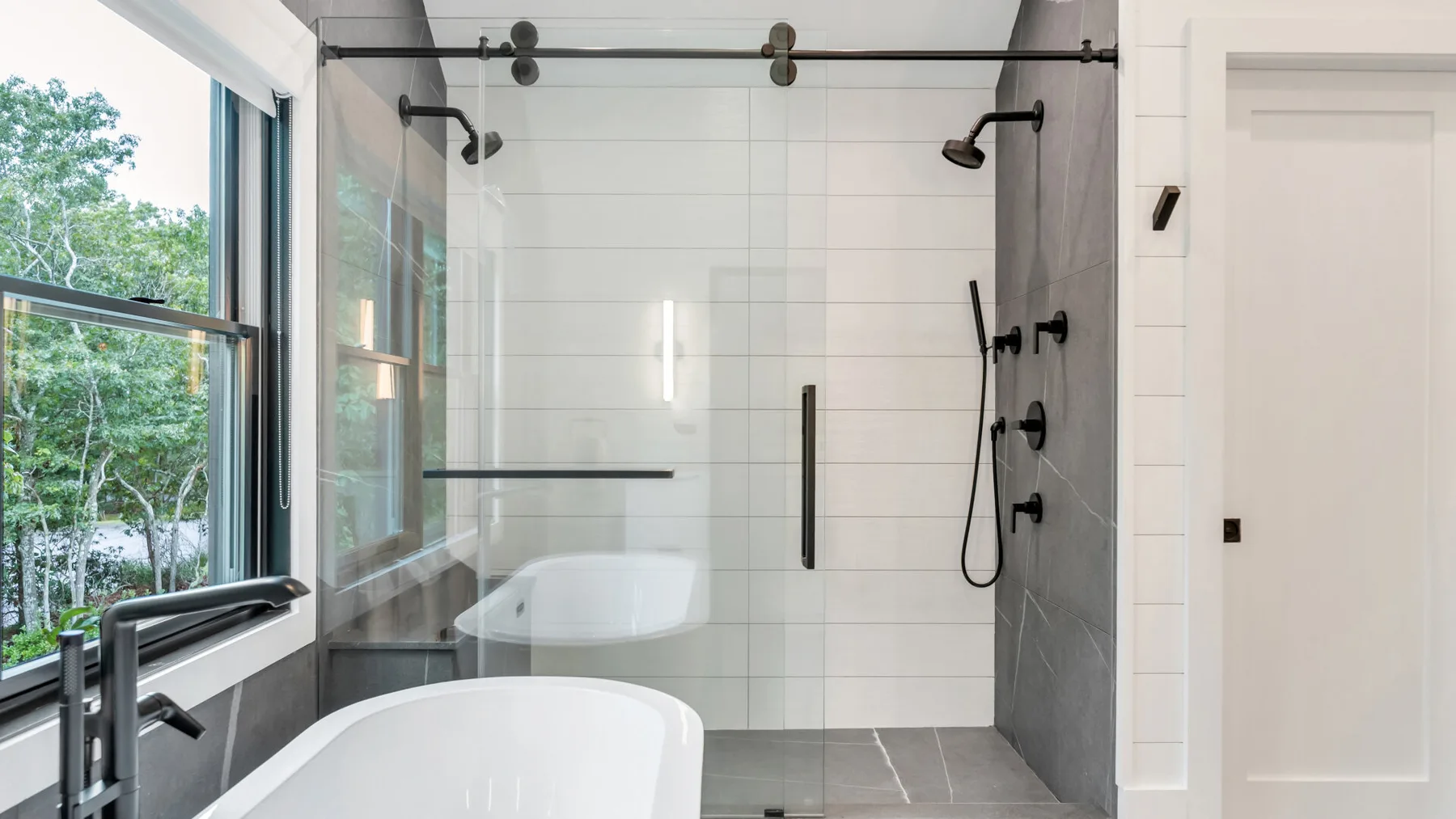 Un baño con azulejos, una ducha de cristal y una ventana grande.