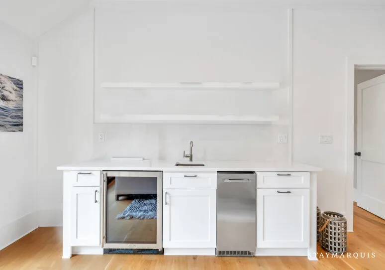 Una pequeña cocina blanca con fregadero, armarios y un electrodoméstico de acero inoxidable.