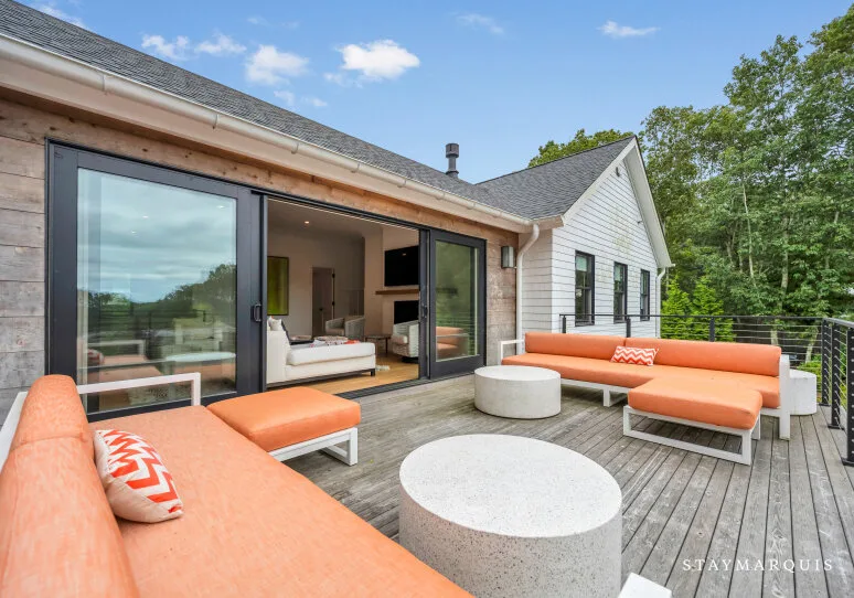 Una terraza de madera con asientos naranjas y vista al salón.