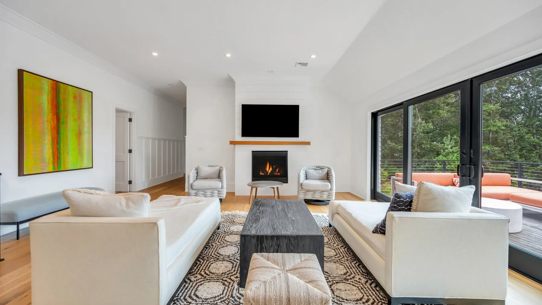 Una sala de estar luminosa con asientos blancos, una chimenea y grandes ventanales.